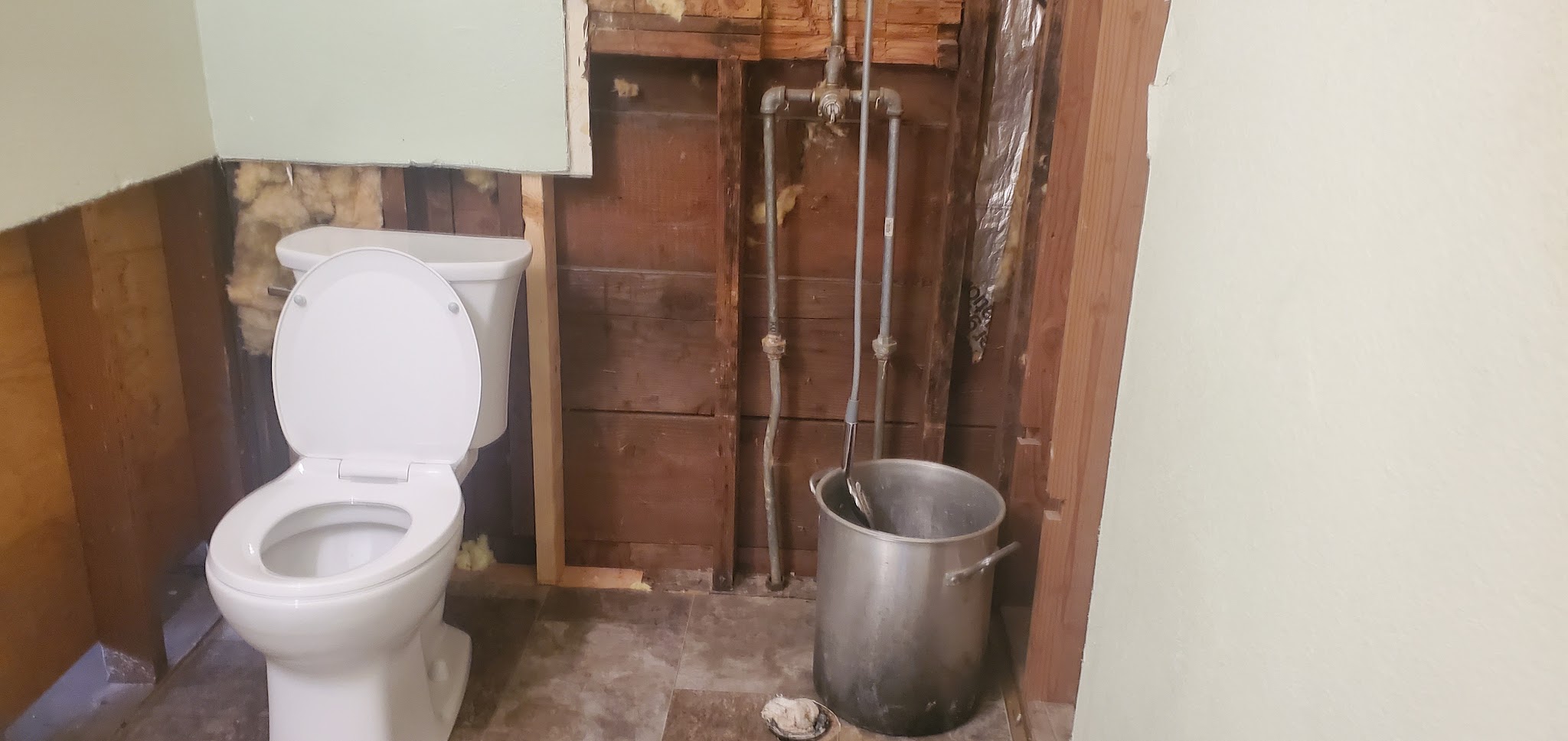 A bathroom mid remodel with the wall opened up, exposing old galvanised supply pipes behind the toilet