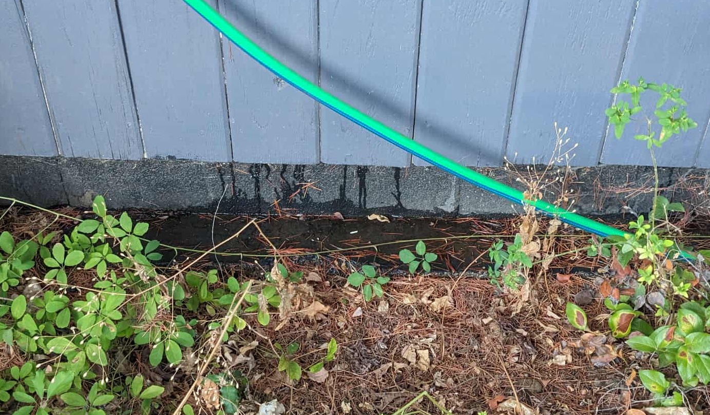 A new water service line run along the outside of a building at foundation level